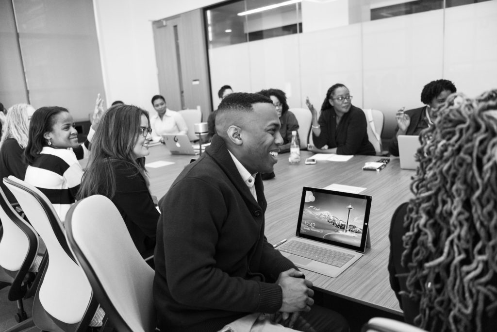 A black and white photo of people sitting an a conference room table, participating in a meeting